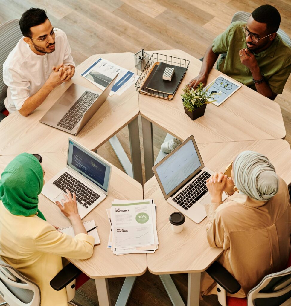 A diverse group of professionals engaged in discussion around a wooden table, focusing on laptops and documents.